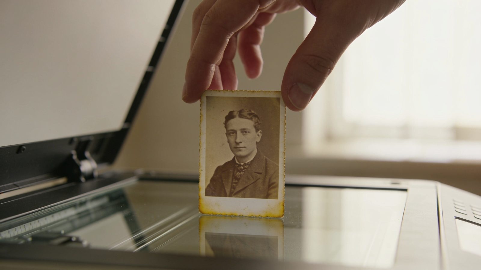 Een hand legt een oude sepiakleurige portretfoto op de glasplaat van een flatbedscanner.